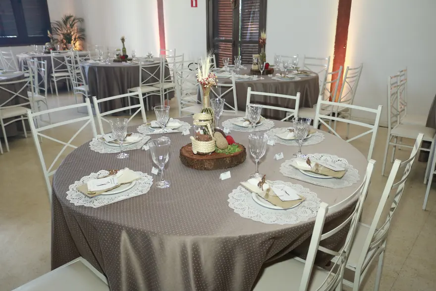 Mesa posta de convidados em um casamento, com pratos, taças, guardanapos de tecido e centro de mesa rústico.