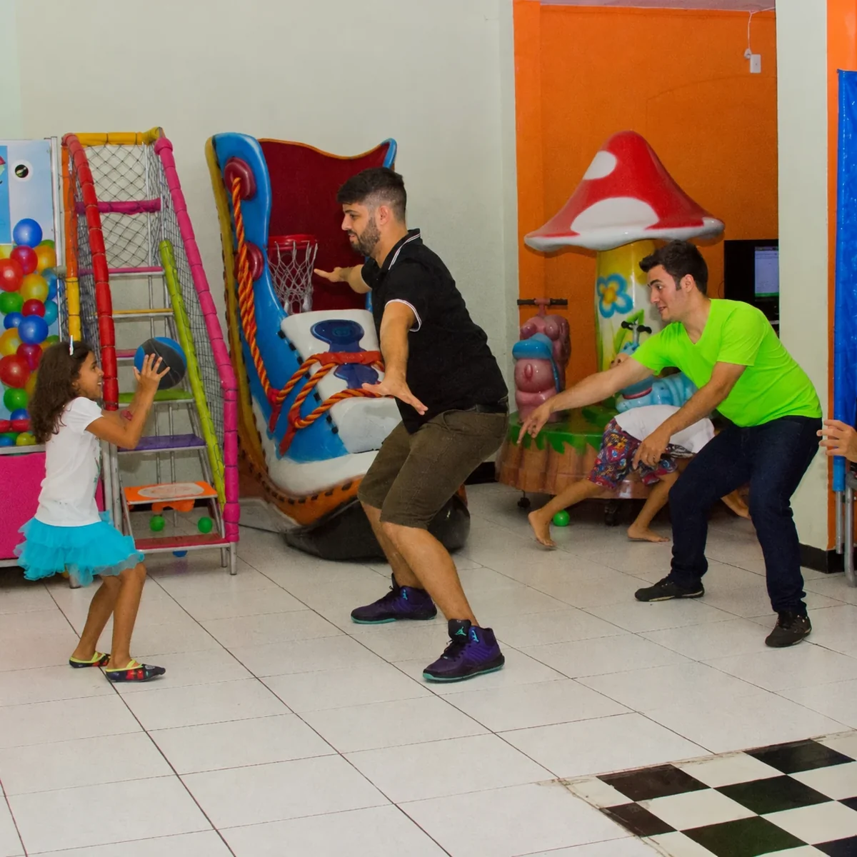 Adultos e crianças brincando com uma bola junto aos brinquedos do buffet infantil.